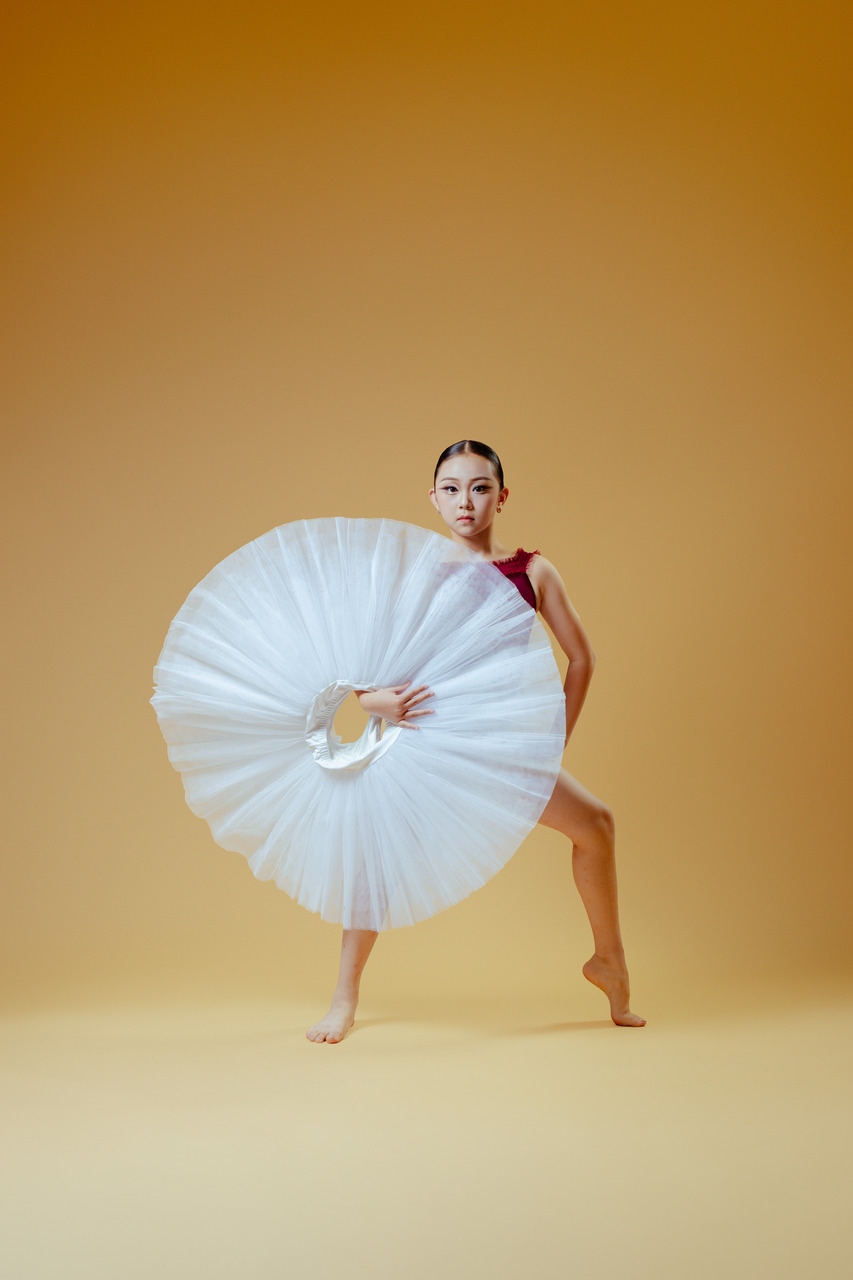A ballet dancer holding a white tutu in front of her in a studio portrait.