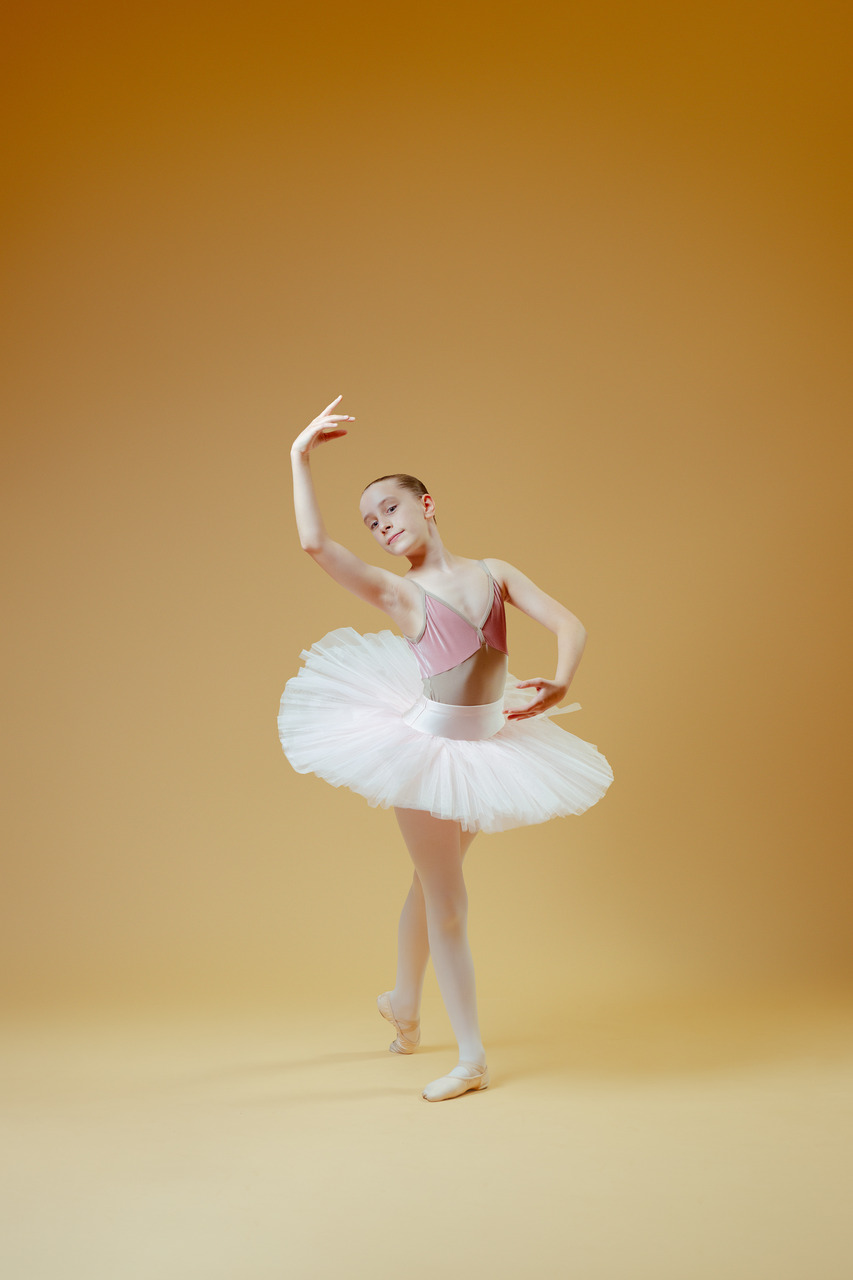 A ballet dancer in a pink leotard and white tutu posing en pointe in a studio portrait.